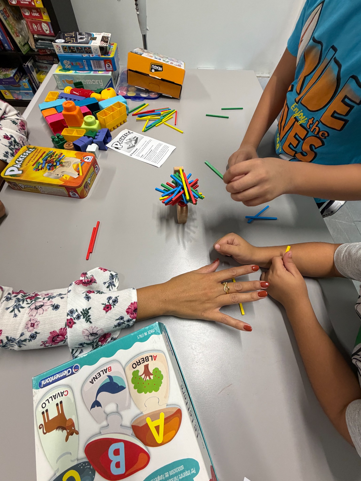 Due bambini condividono un gioco al tavolo con il sostegno delle mani di un adulto
